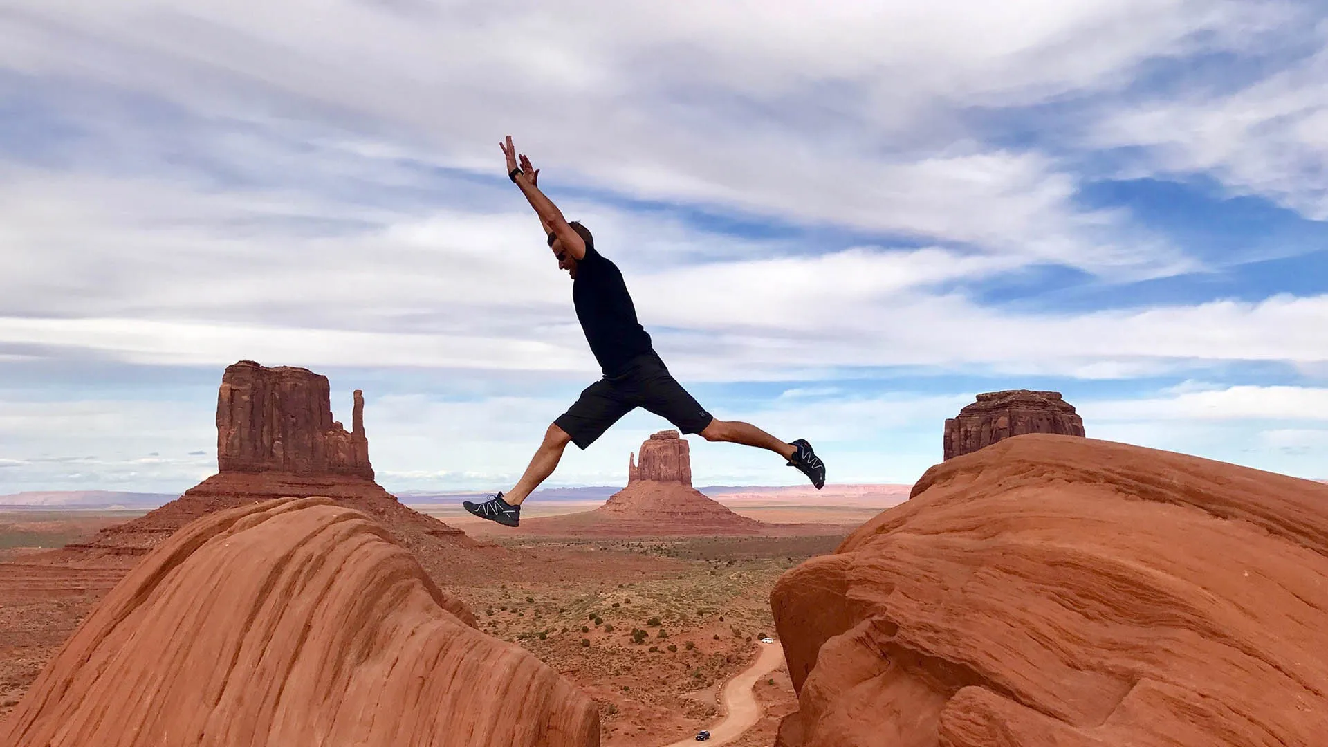 person jumping from one rock to the other with the monument valley in background