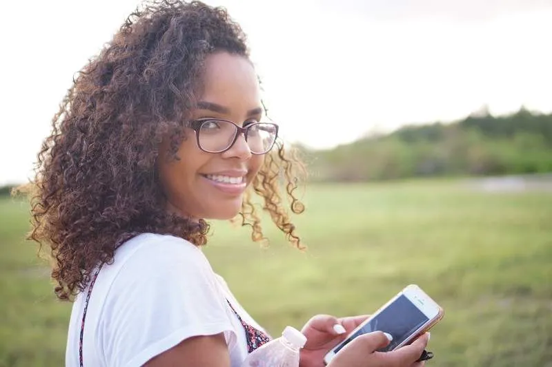 a young woman smiling and holding her cell phone