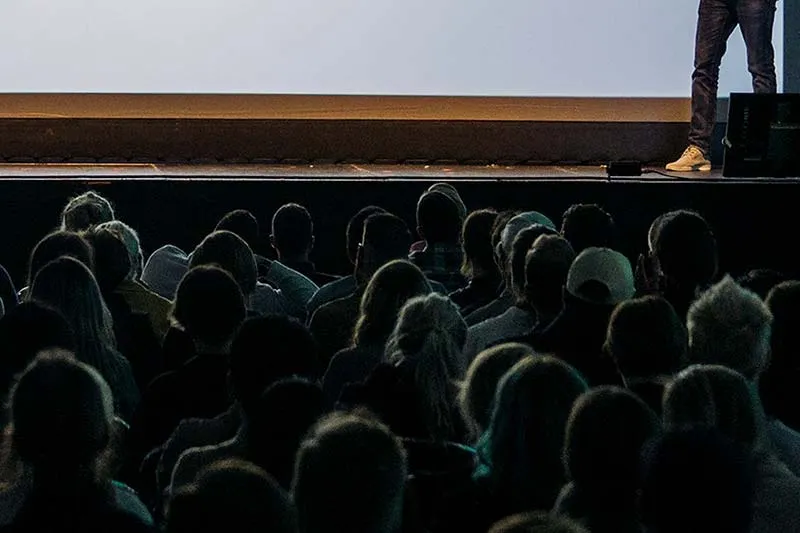 men and women standing by and sitting at a table looking at a laptop