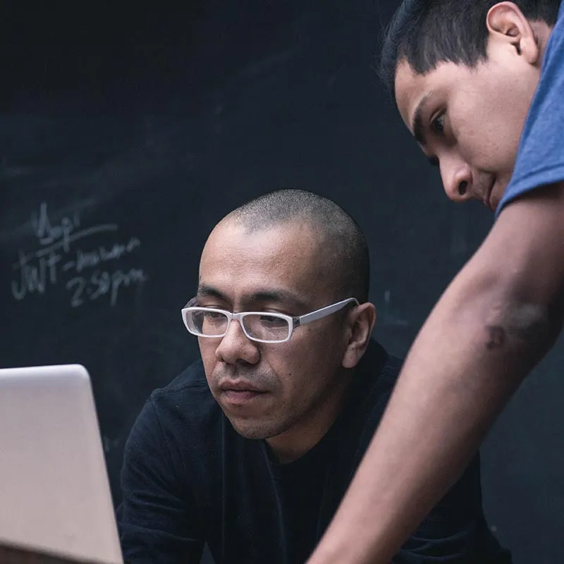 man teaching another man working on a laptop how to do something 