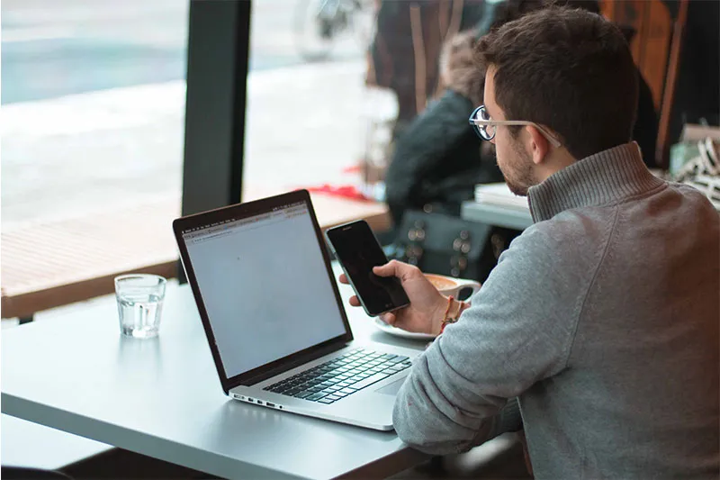 man at table using laptop and mobile phone