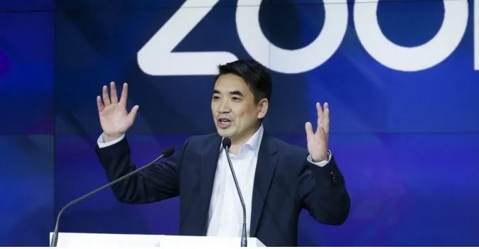 founder and ceo of zoom eric yuan giving a presentation in front of giant blue screen with zoom written on it