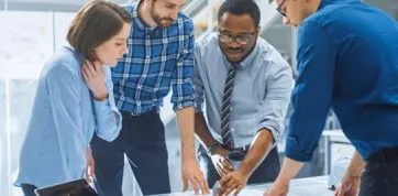 four colleagues working together standing at a table looking at a plan for innovation