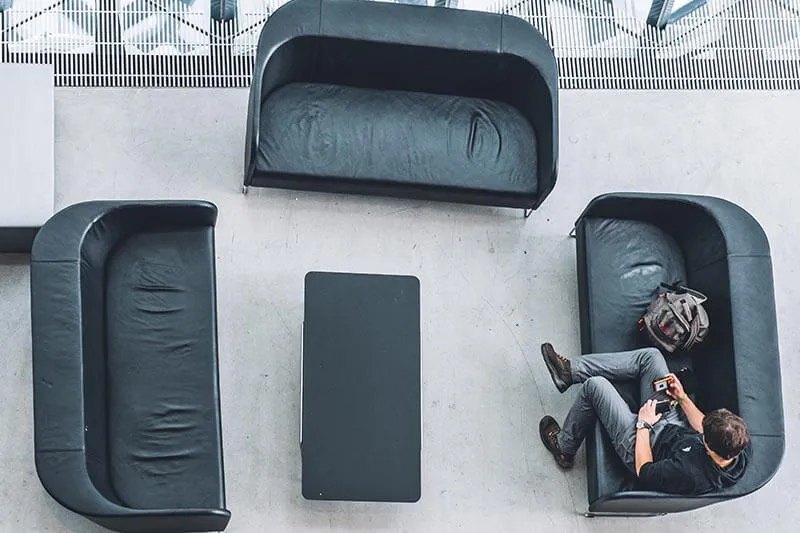 a young guy sitting on a couch inside a building looking at his phone