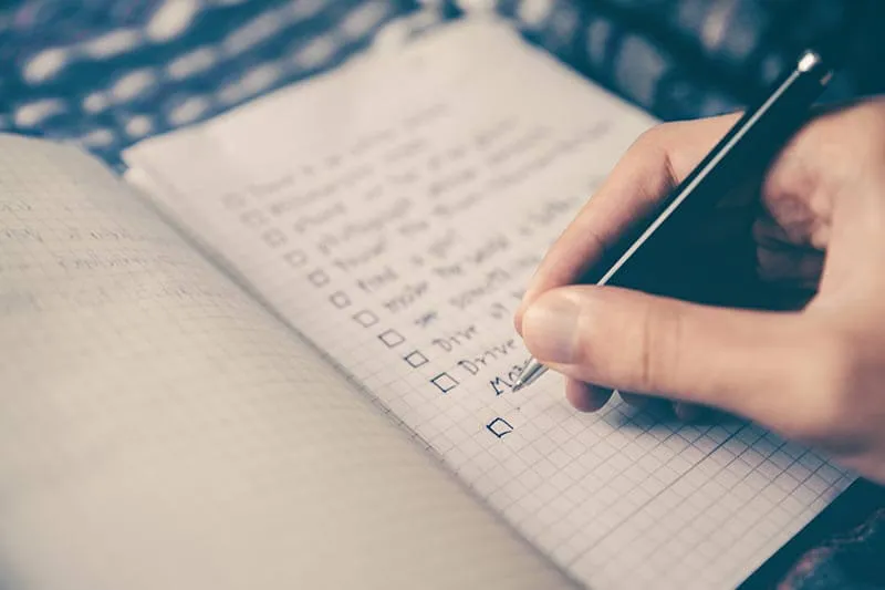 a person writing a checklist on a notebook