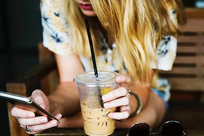 a girl sipping coffee and checking her cell phone