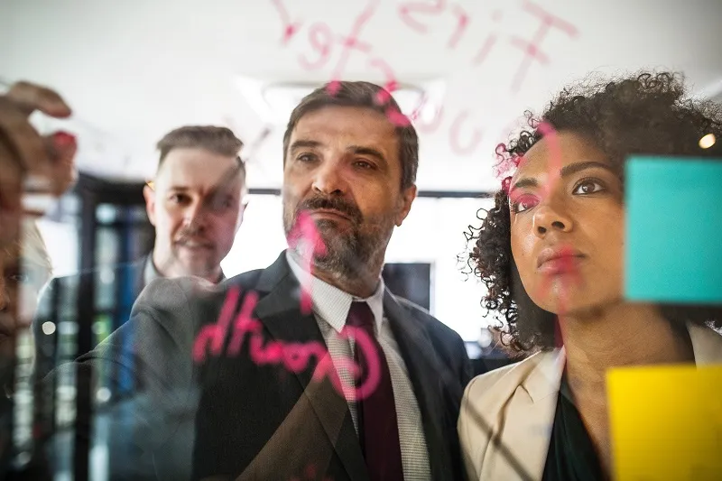 instructional designers in a meeting room writing text on a transparent board