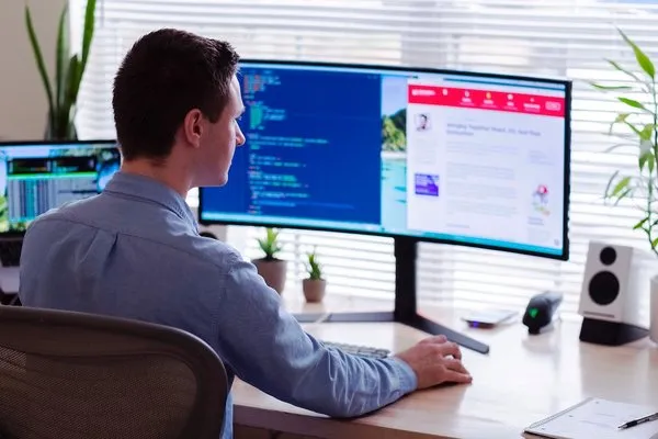 businessman from home sitting at desk in front of laptop and computer screen