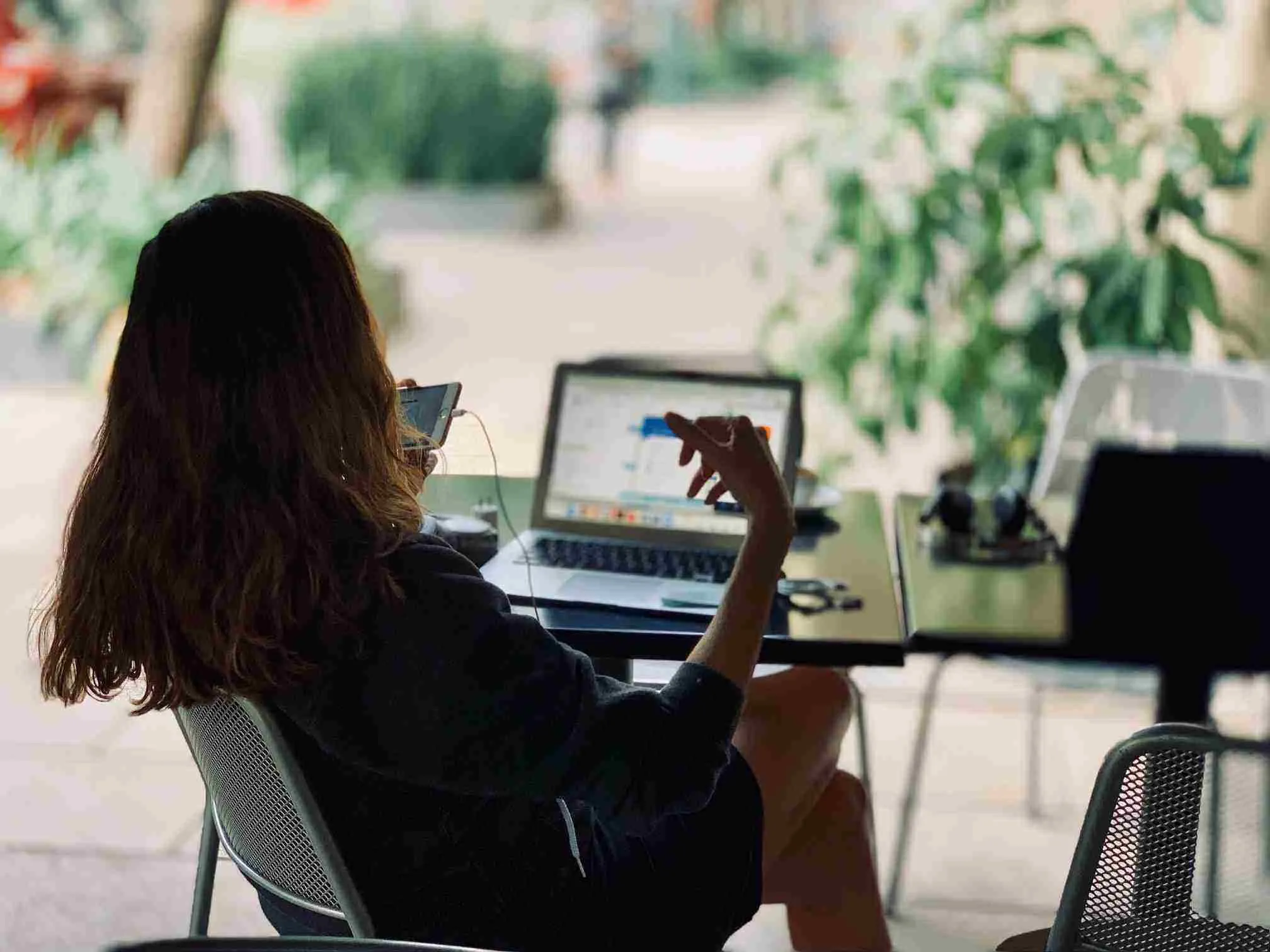 woman working remotely on her laptop at a table while also looking at her smartphone