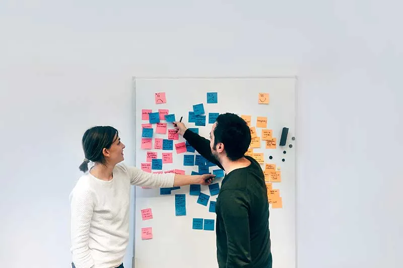 two people working on a customer journey map to improve human experience using a white board and sticky notes 